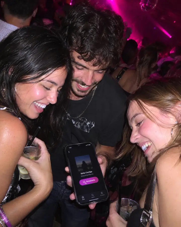 Tres amigos en la pista se ríen mirando un móvil con su canción «Aceptada».