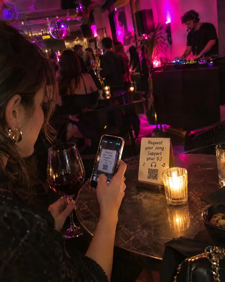 A cocktail bar with a DJ in the corner and a guest scanning the QR code with her phone.