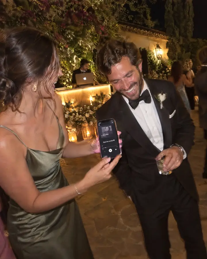 Invitados y novios bailando en una boda de noche mientras alguien sostiene un móvil.