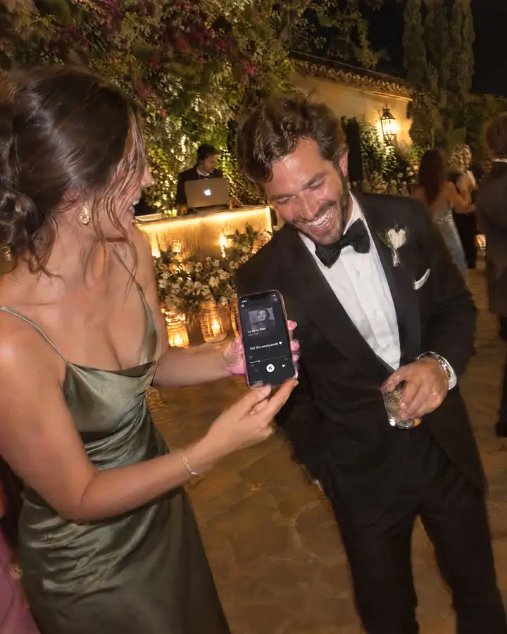 Guests and the couple dancing at a wedding at night while someone holds a phone.