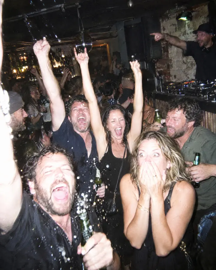 Flash photo in a small bar: a group of friends scream with their arms up the moment their song starts, and the DJ points at them.