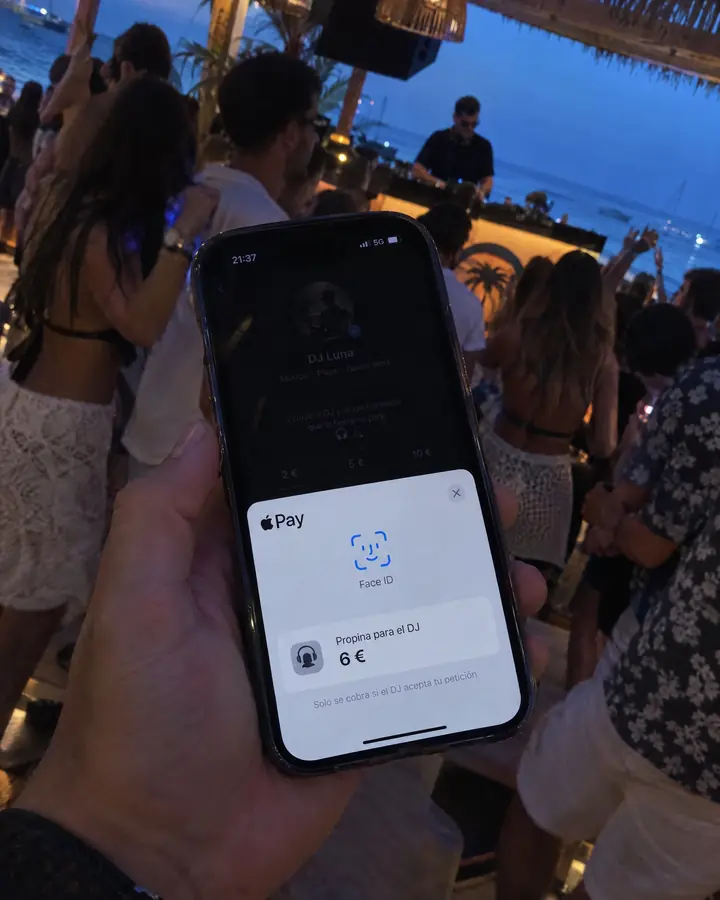 En un beach club, el móvil enseña la hoja de Apple Pay con la propina para el DJ y el aviso de que solo se cobra si la acepta.